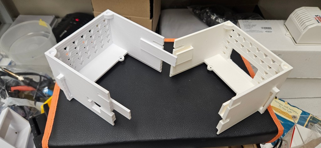 The image depicts a white 3D-printed object, possibly a model of a house or room, placed on a black surface with orange tr...