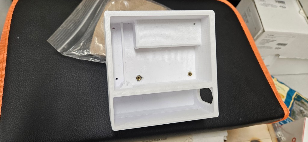 A white plastic object with a rectangular shape, featuring a small rectangular section and two gold screws at the bottom, ...