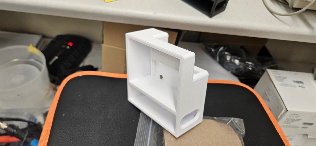 The image depicts a white, rectangular object with a hollow interior, situated on top of a black and orange cushion, in fr...