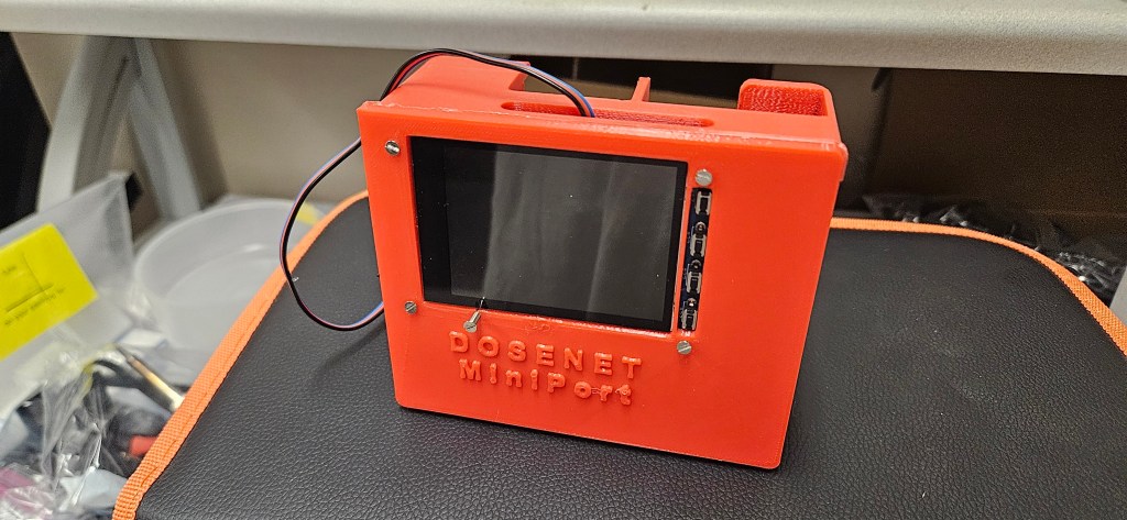 The image depicts a small, rectangular device with a screen and wires attached to it. The device is likely a type of compu...