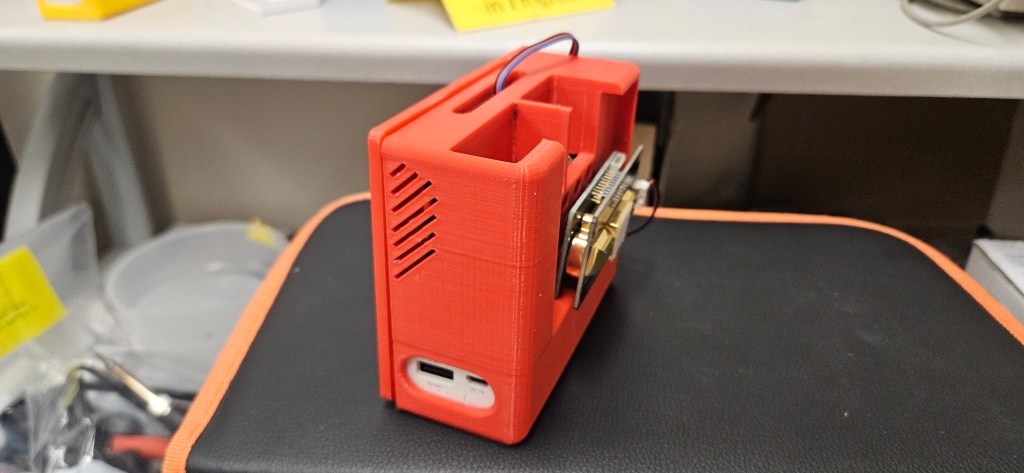 A 3D printed red box with a black and orange cushion, sitting on a white table.