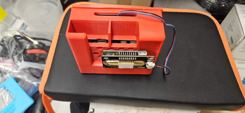 The image shows a small, red plastic box with various components inside, sitting on top of a black and orange table or sta...