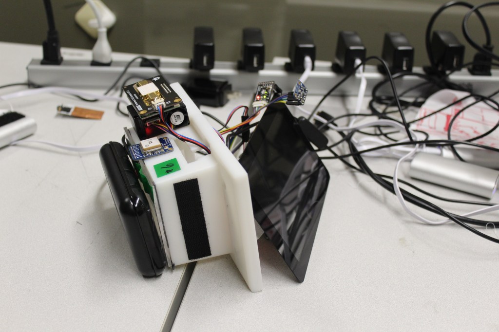 The image depicts a white, rectangular device with various components attached to its surface. The device appears to be a ...